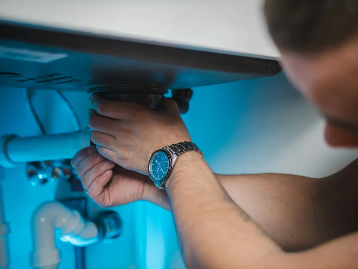Plumber fixing pipes under a sink during a home service visit