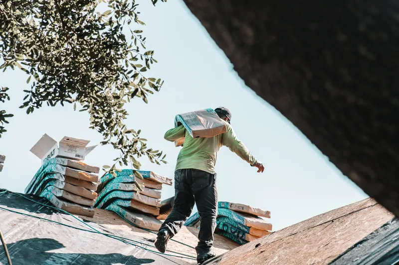 Roofer carrying a bundle of shingles across a residential roof