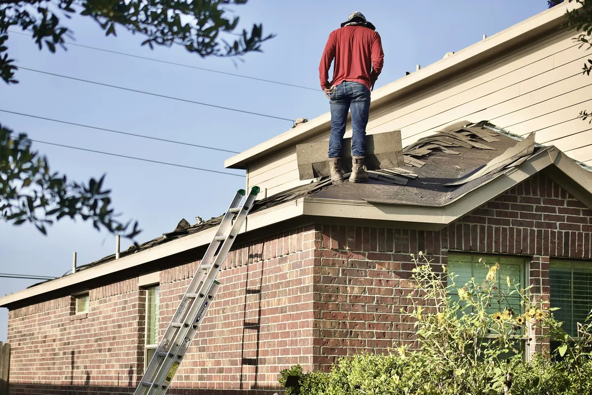 Roofer standing on the roof of a brick suburban home during a roof replacement